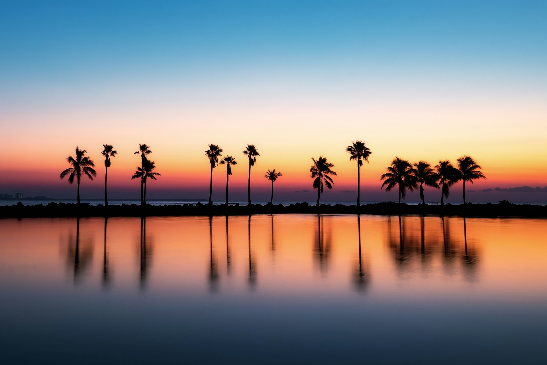 Tropical sunset with palm trees reflected on calm water